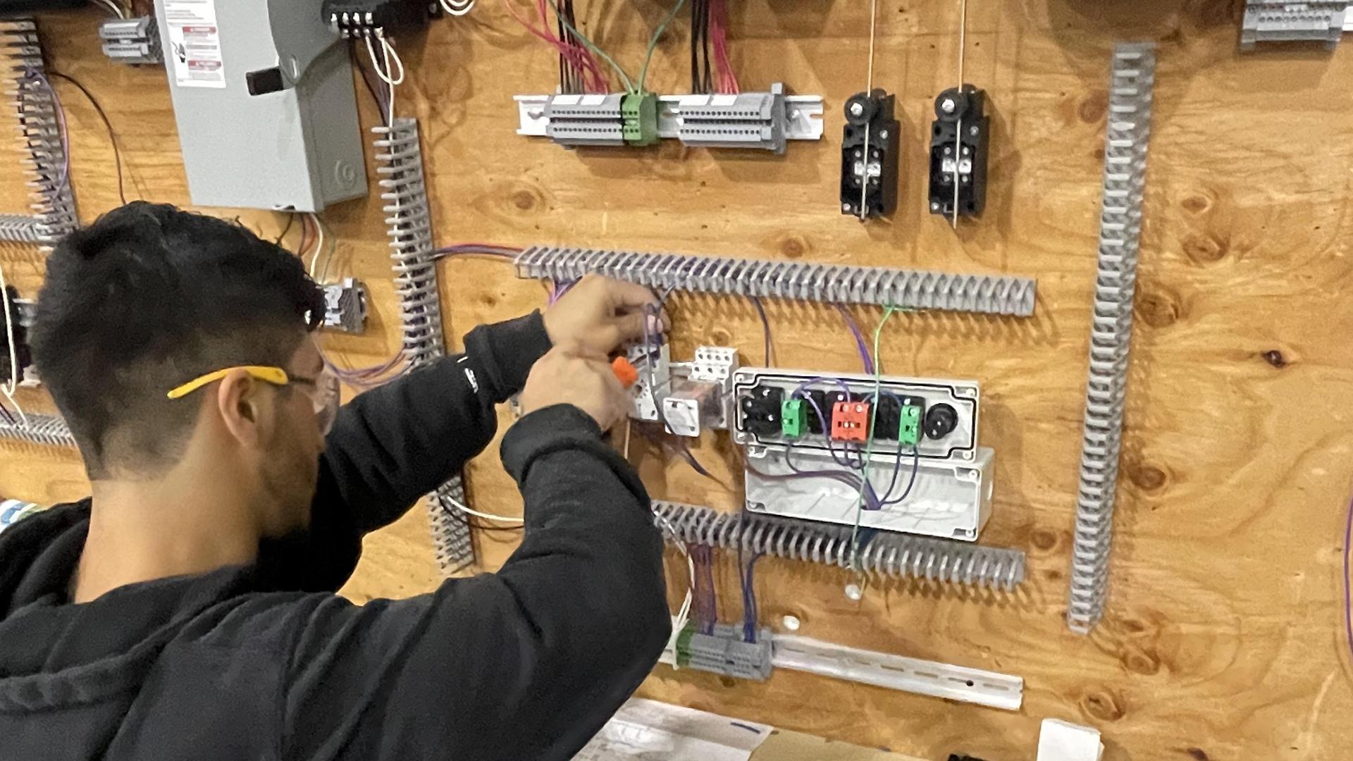 Person working with electrical components on a wall in a workshop environment.