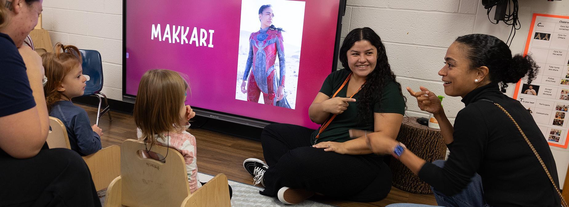 Preschool classroom with teachers and students, Ridloff and screen with her character in Eternals