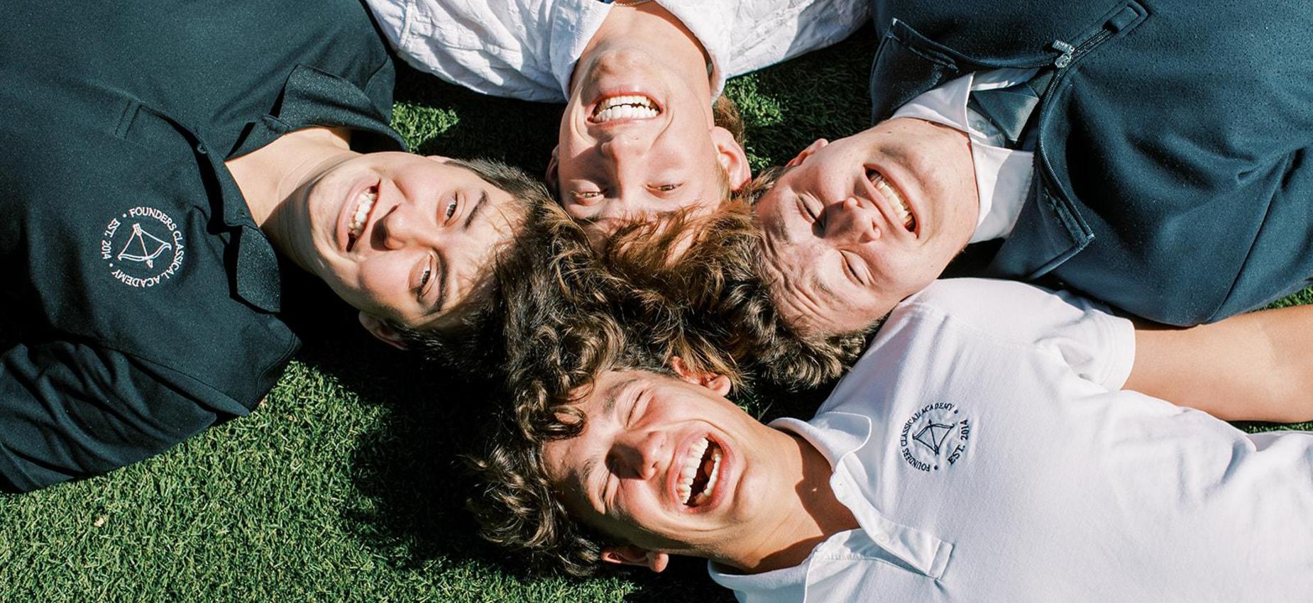 Four smiling high school students lie in a circle on the grass