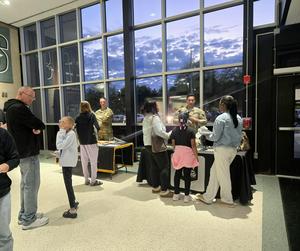 People gather near tables in a school lobby, with soldiers discussing information.