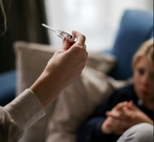 Adult hand holding thermometer in foreground with sick child in the background