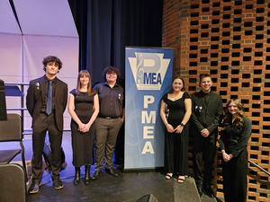 students dressed in black stand on stage around PMEA sign