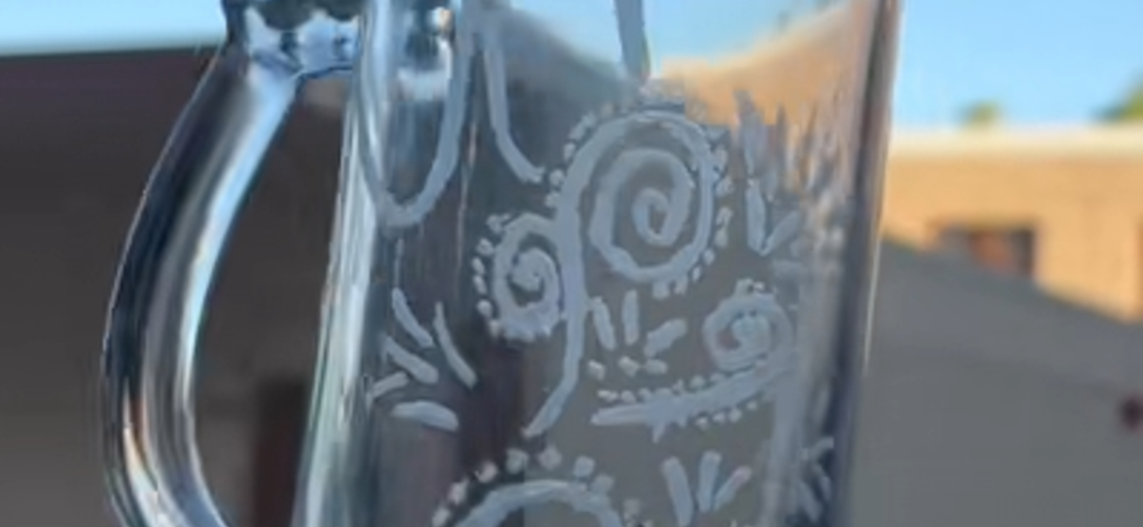 A decorative glass pitcher with swirling patterns, against a blurred outdoor background.