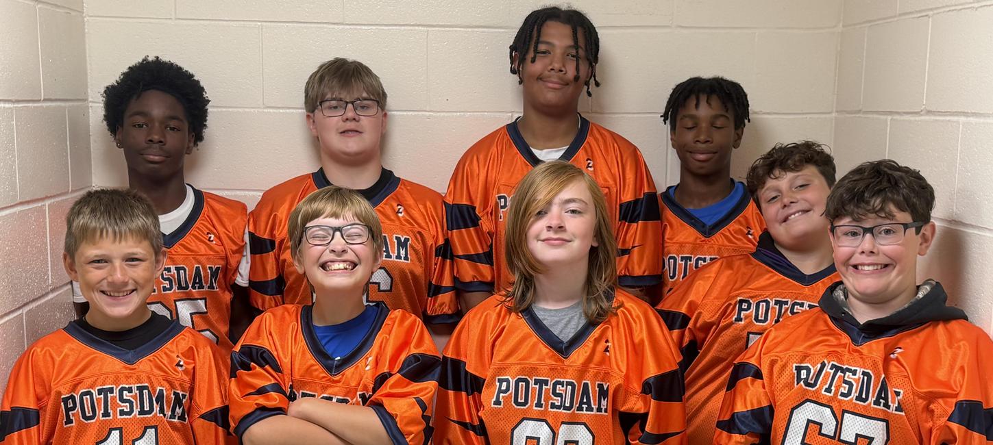 A group of students in orange jerseys smile in a hallway