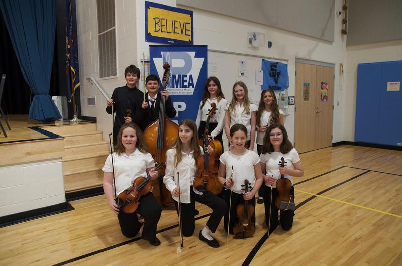 string students standing in front of stage holding instruments