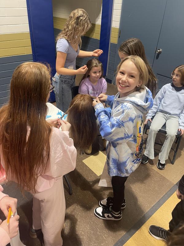 girl smiling at camera while braiding hair of another student