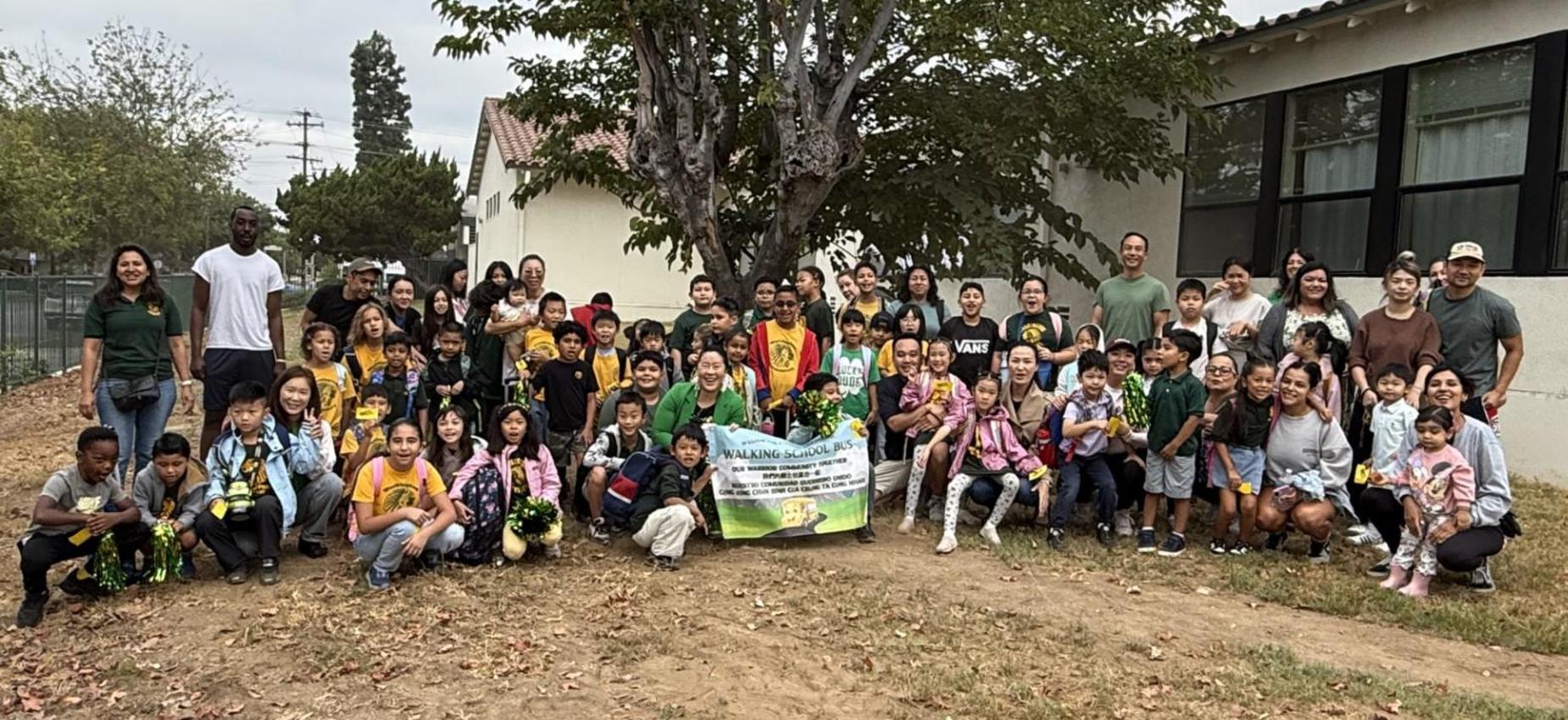 A large group of children and adults posing together outdoors under a tree.