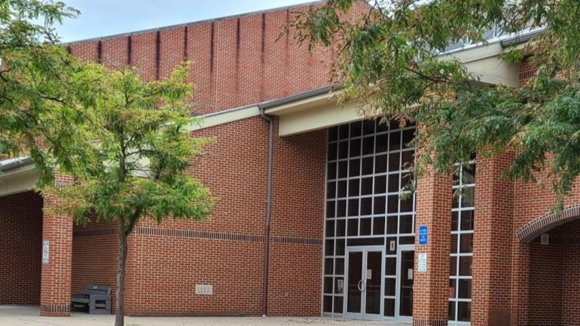 Brick building with large windows and green trees in front.