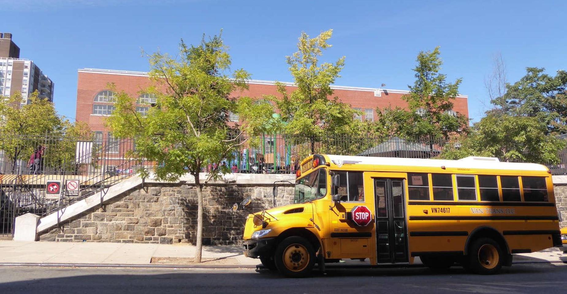 Yellow school bus parked outside a brick school building with trees.
