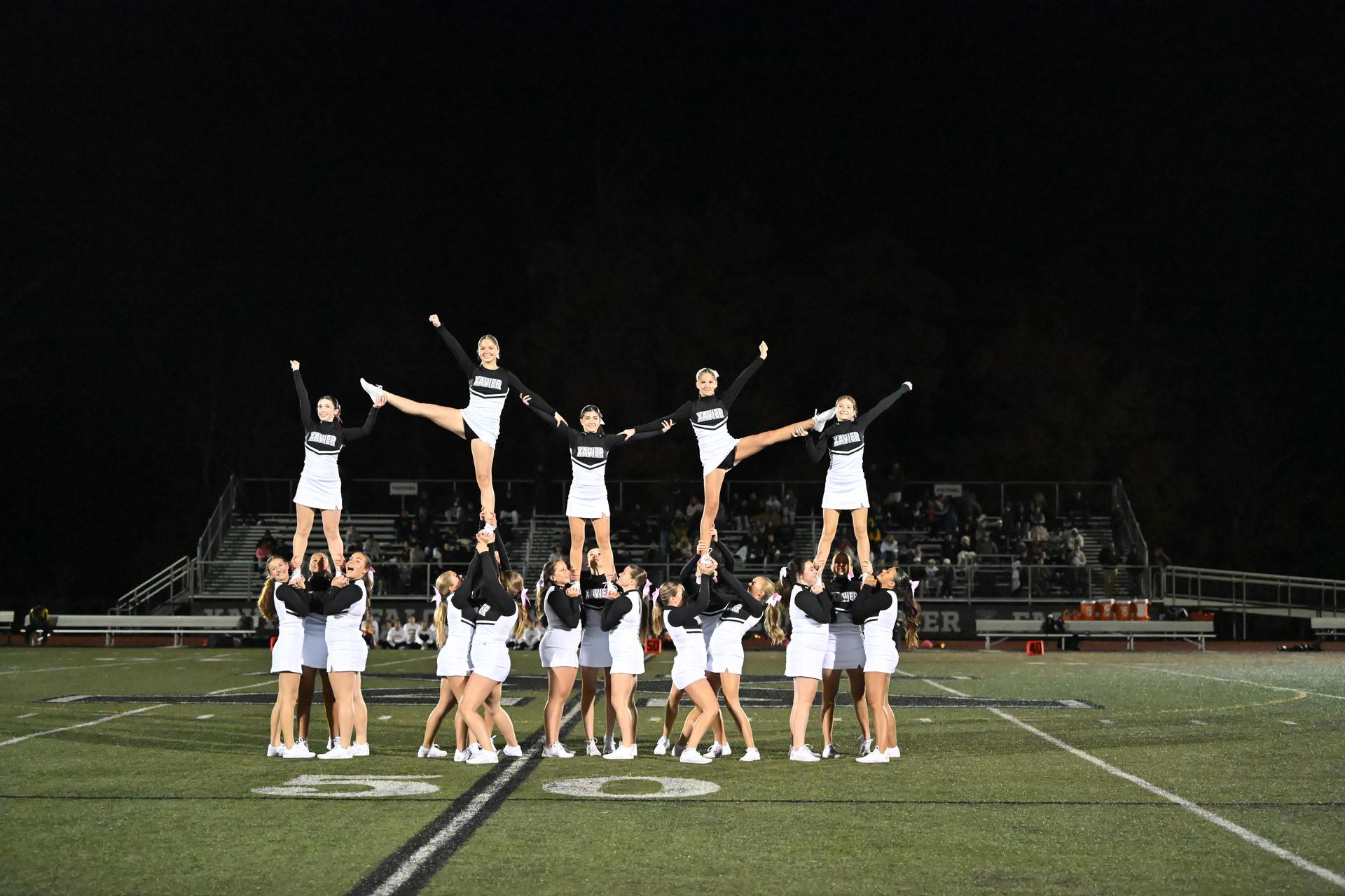 Cheerleaders performing a pyramid stunt at night on a football field.