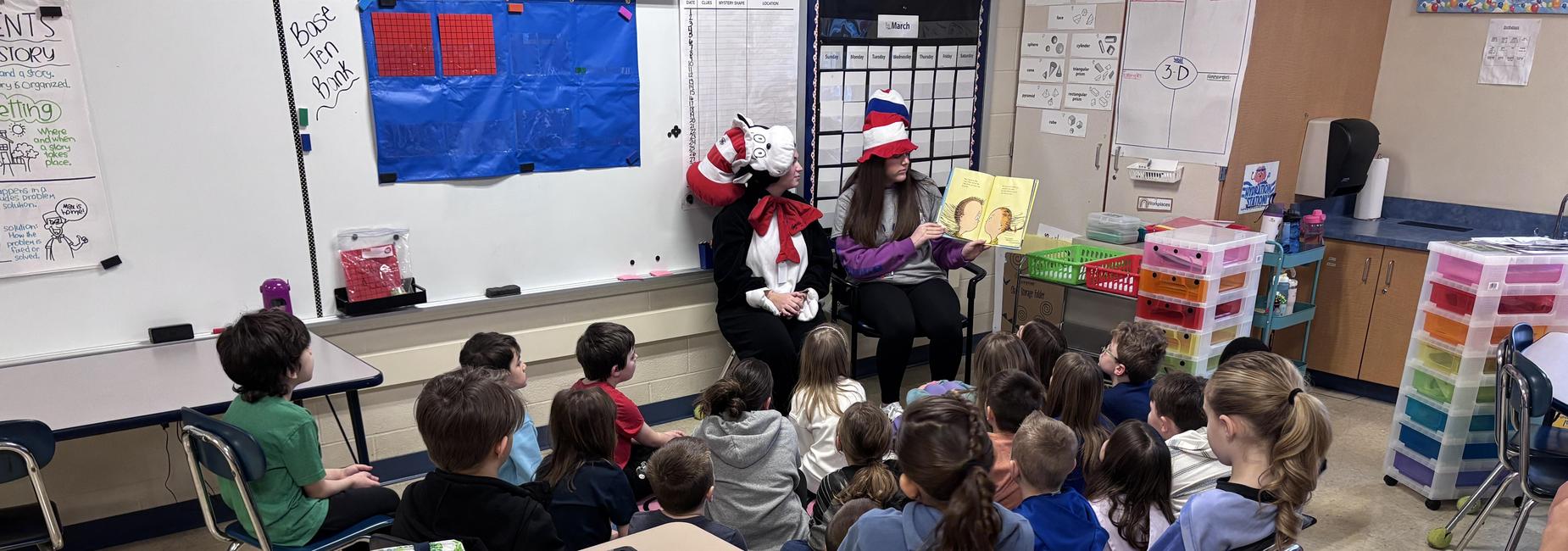 Students in chairs listening to guest speaker reading a book.