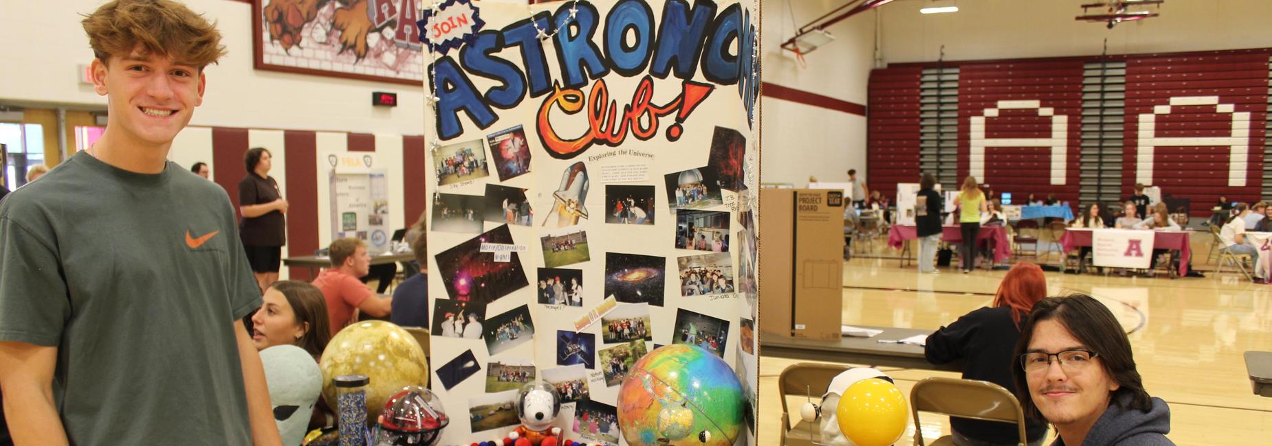 Two students smiling at a science fair booth with globes and science displays.