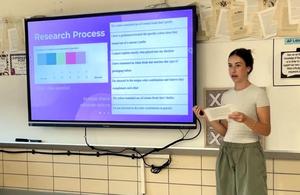 Student explaining a research process in front of a classroom screen.