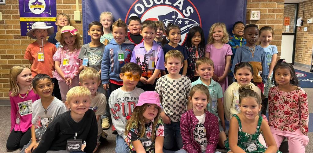 A large group of smiling children posing together in front of a school banner.