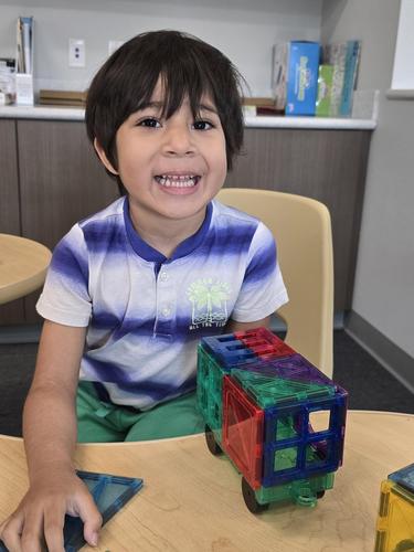 A child smiles while playing with colorful building blocks at a table.