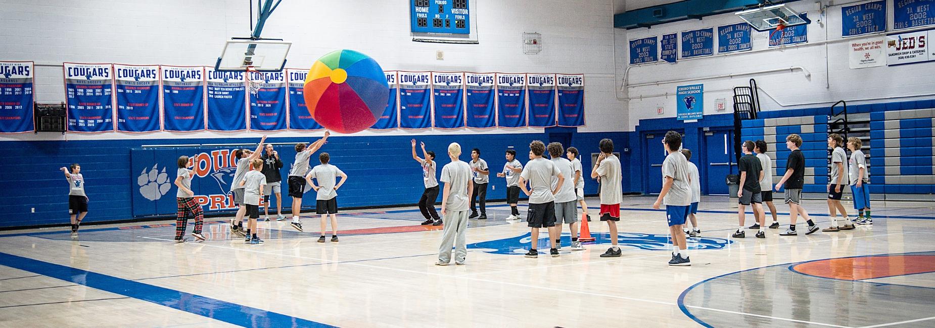 boys pe class in gym with giant beach ball