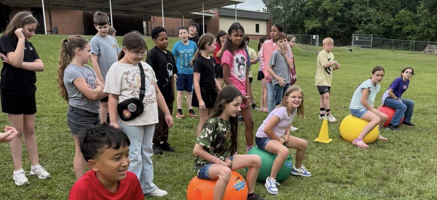 Kids sit on exercise balls in a field, preparing for a fun activity.