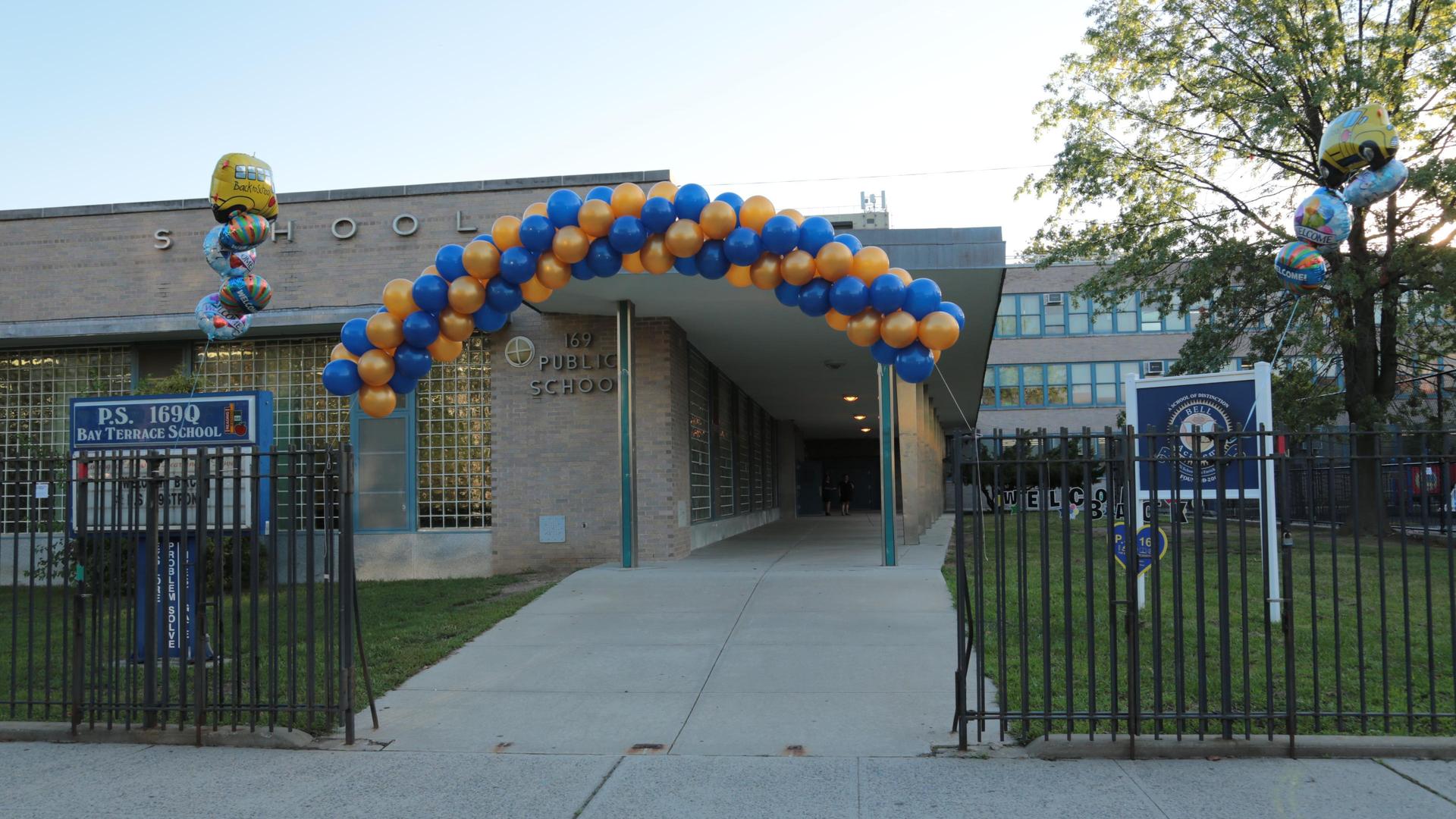 Archway of blue and orange balloons over school entrance with signage.