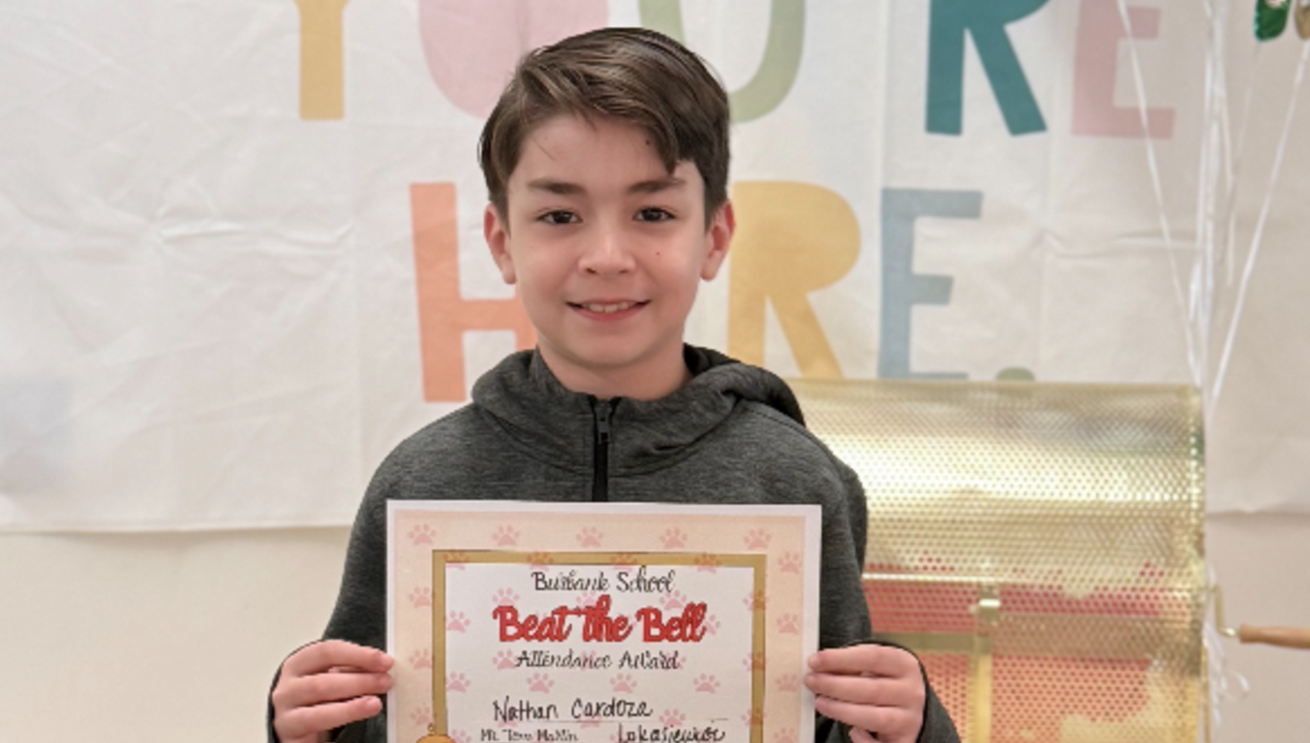 Boy holding an attendance award in front of a colorful backdrop.