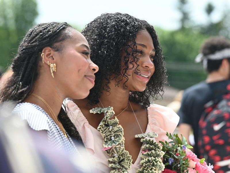 Two young women, one with a floral bouquet, smiling together outdoors.