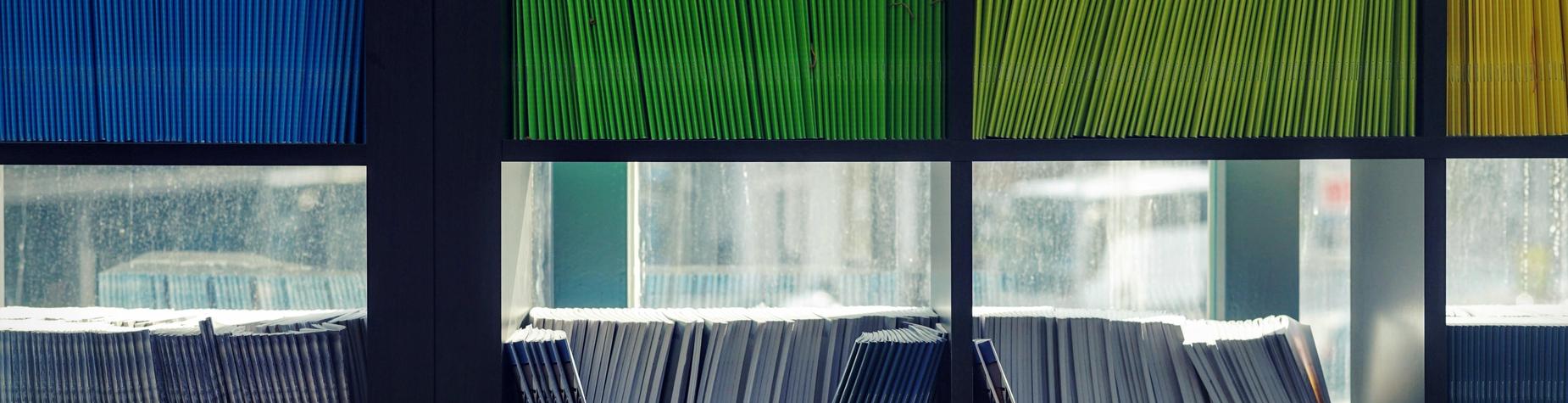 Stacked files in green, blue, and yellow organized in a shelf.