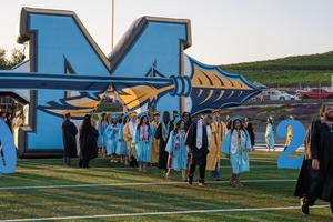 MHS Graduates enter graduation under the M logo