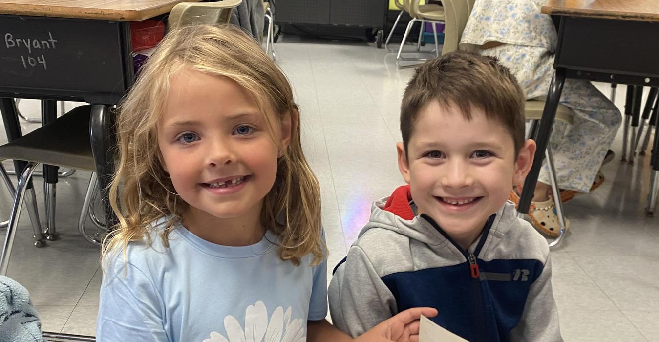 Smiling girl and boy sitting together holding a paper in a classroom.