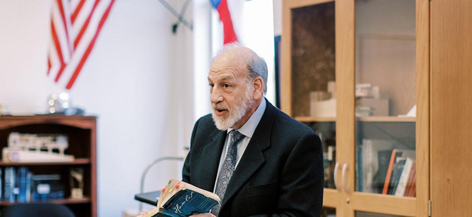 Teacher in a suit smiles while holding an open book