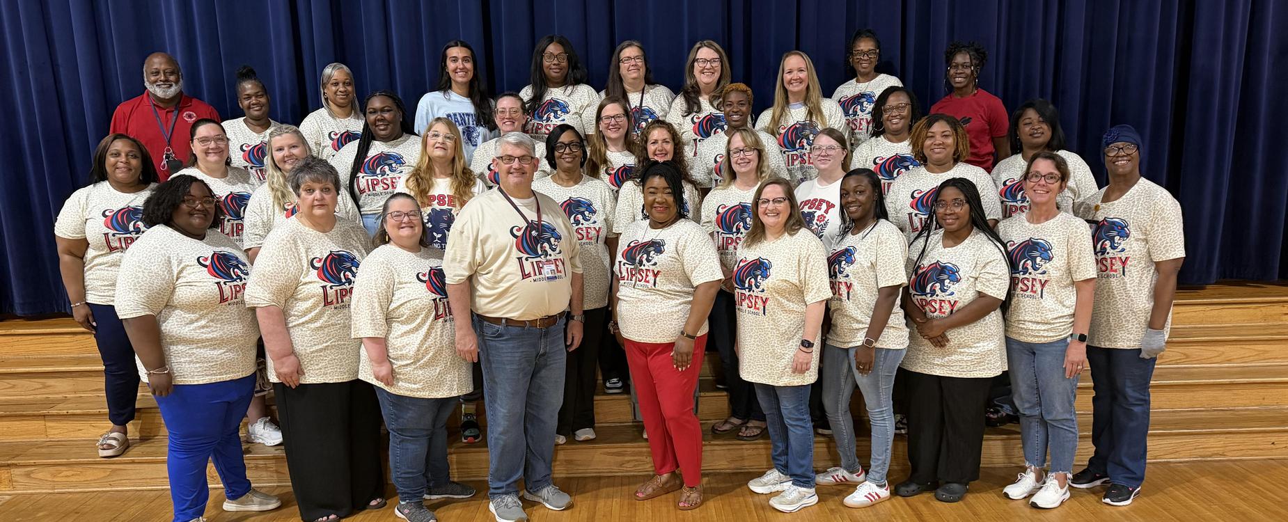 Lipsey staff in matching shirts posing for a photo on a wooden stage.