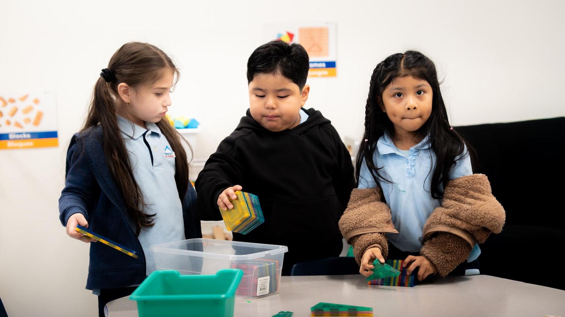 Three children playing with colorful building blocks at a table.
