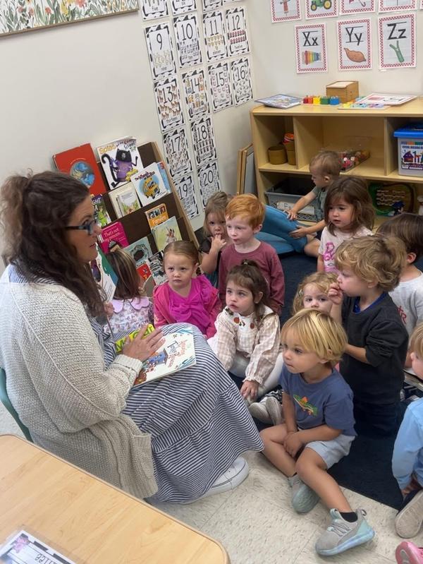 A teacher engages with young students while reading a book.