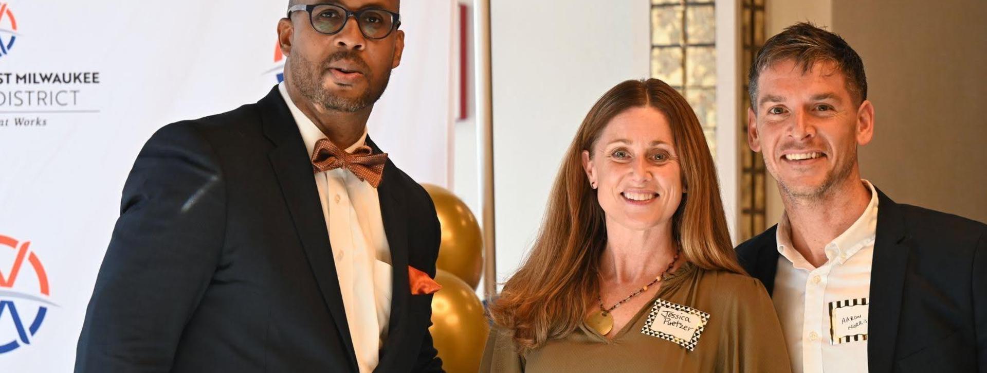 Three people posing together at an event with decorations in the background.