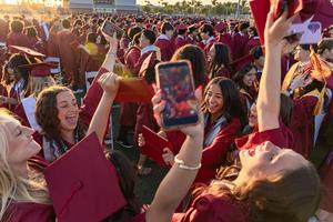 A group of graduates celebrate their milestone achievement by raising their hands and cheering in a circle.