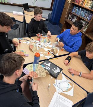 Five students engaged in a crafting activity around a table.