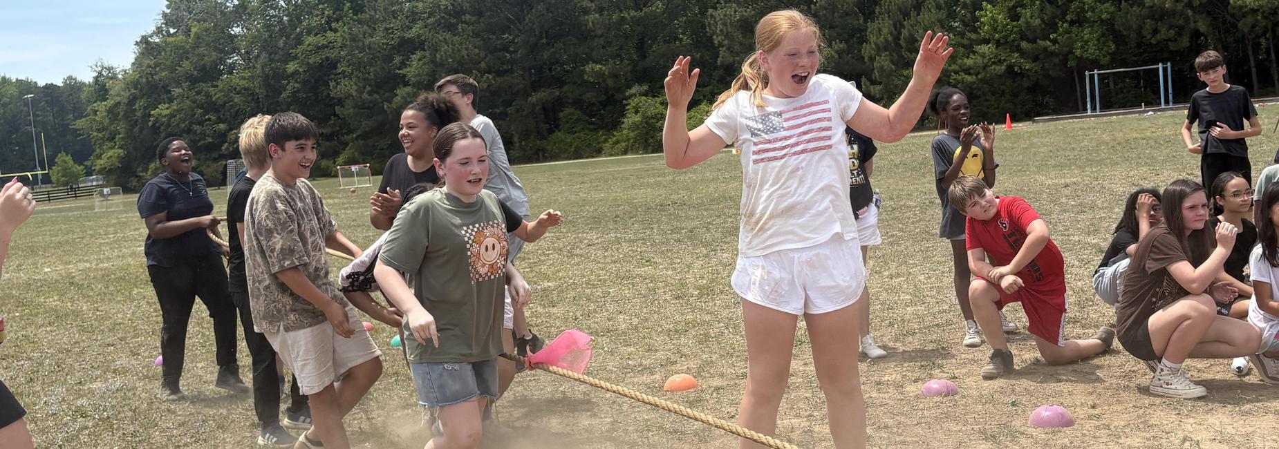 Children participating in a tug-of-war, laughing and cheering on a field.