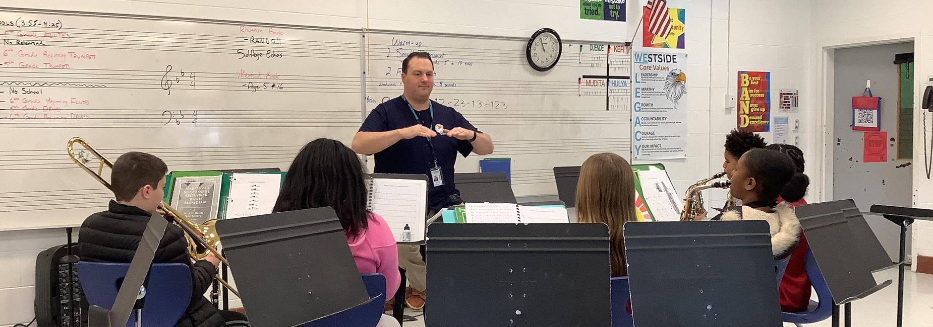 Music instructor leading a band practice session with students seated at music stands.