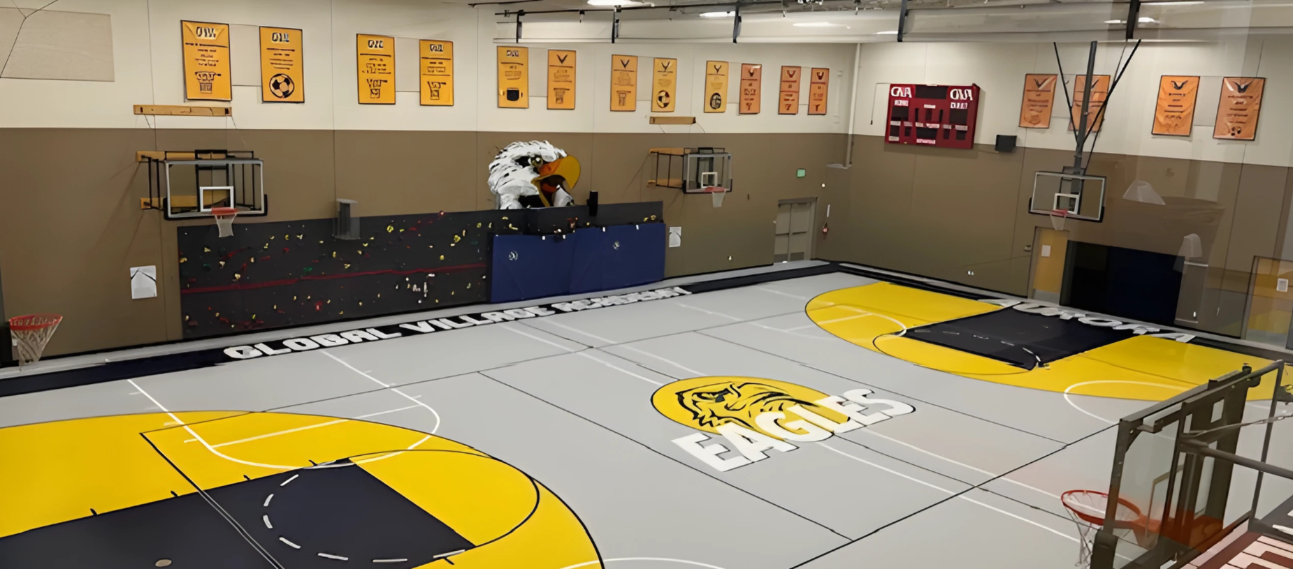 Basketball court with gray and yellow markings, eagle mascot, and wall banners.