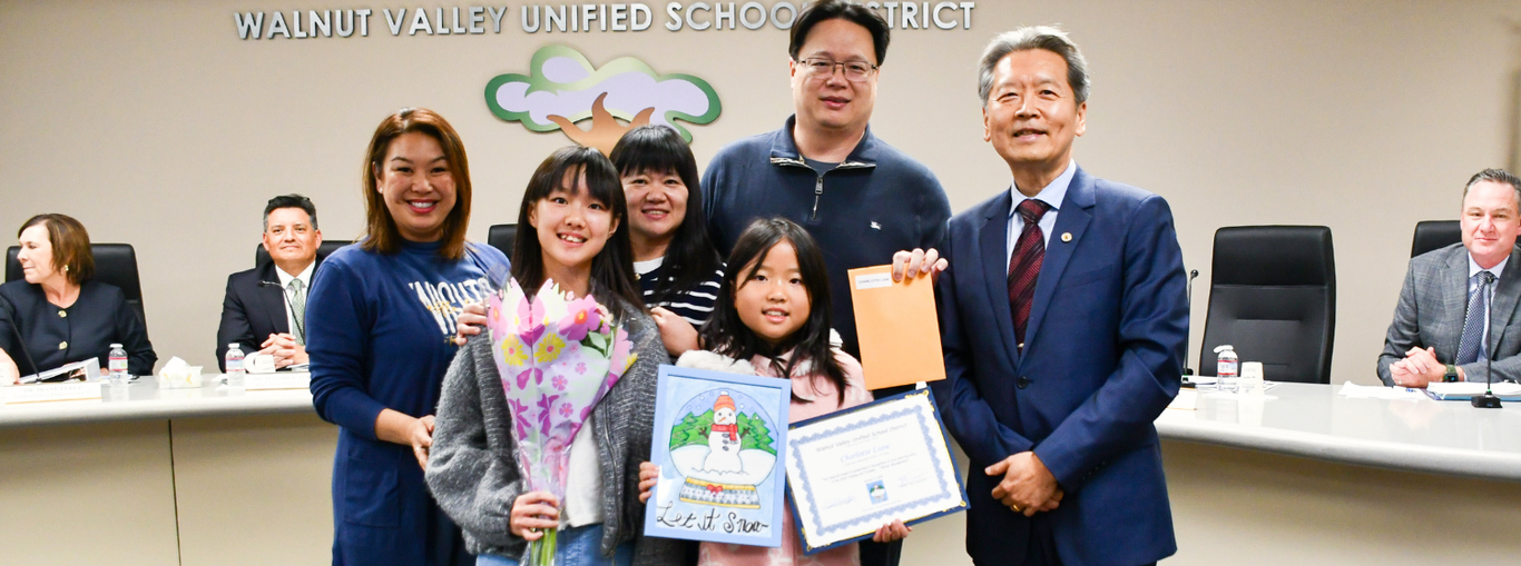A family with children presenting awards and flowers during a school meeting with officials.