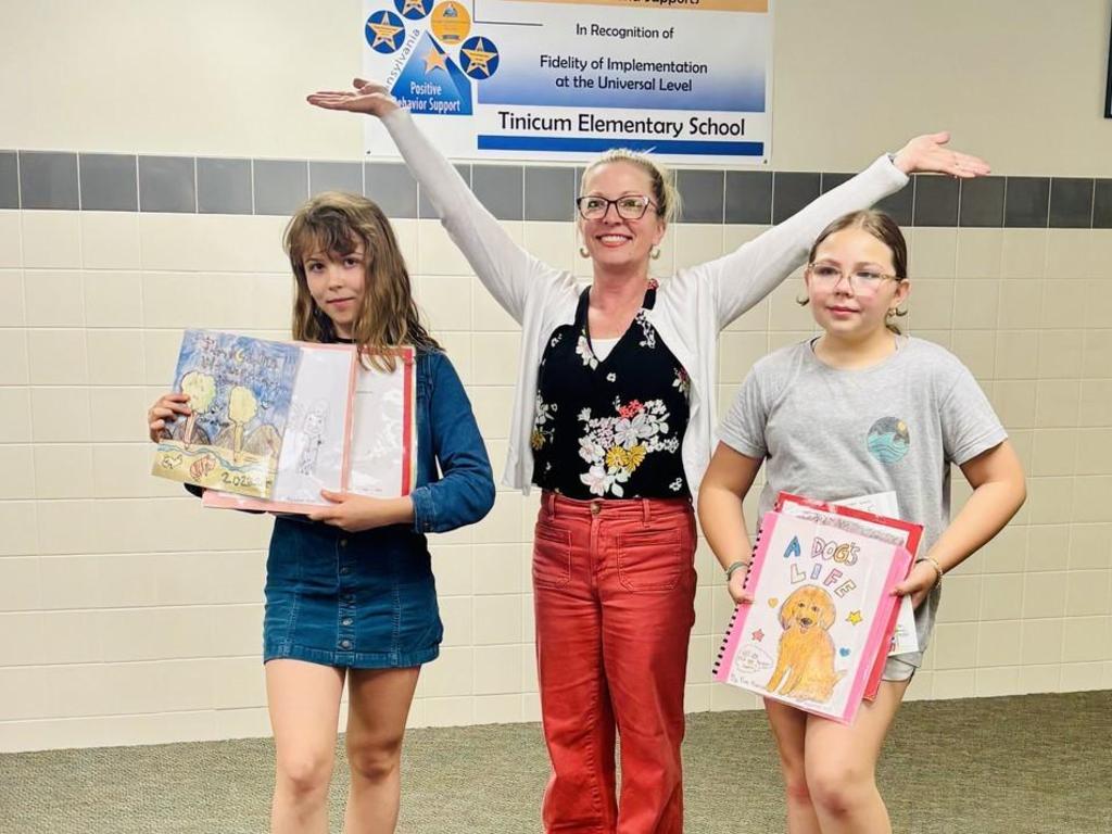 Mrs. McNichol standing with two students who are showing off the new books they just published.