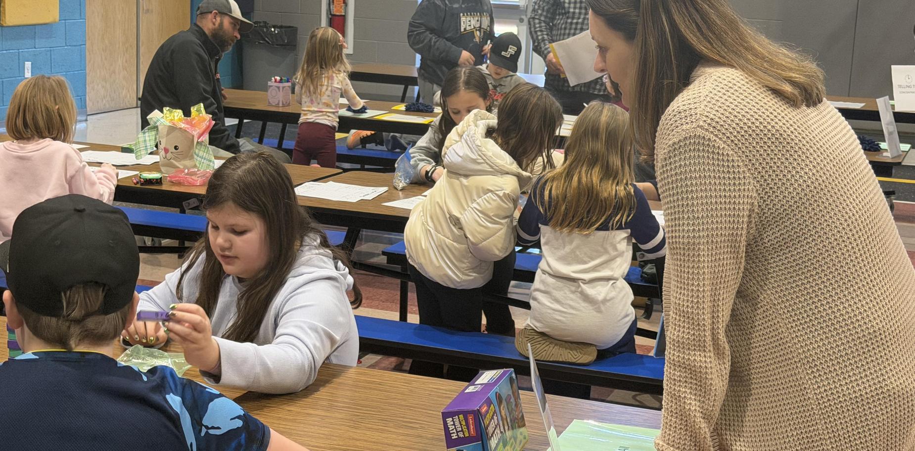 Children and adults engaged in activities at tables in a school setting.