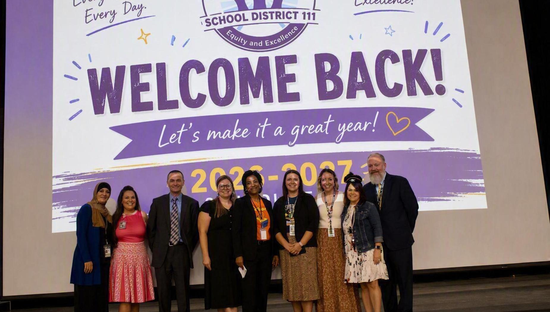 A group of nine people standing in front of a large welcome banner.