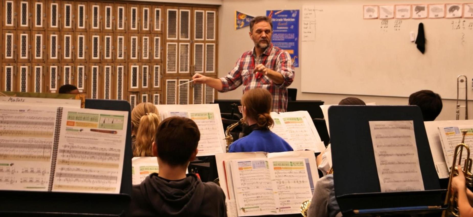 A music teacher conducting a youth band with sheet music visible.