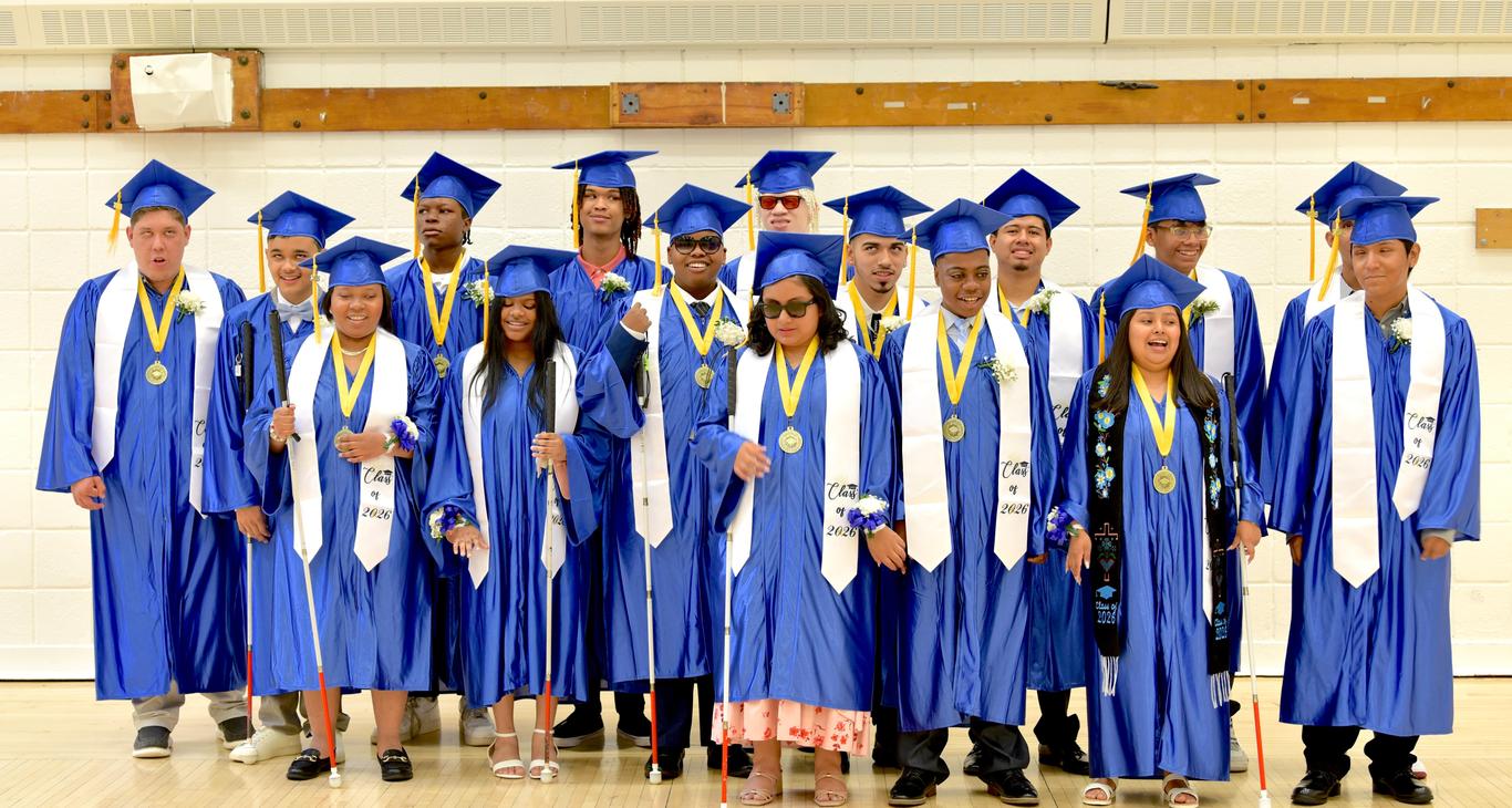 Group of graduates in blue caps and gowns, smiling and celebrating.