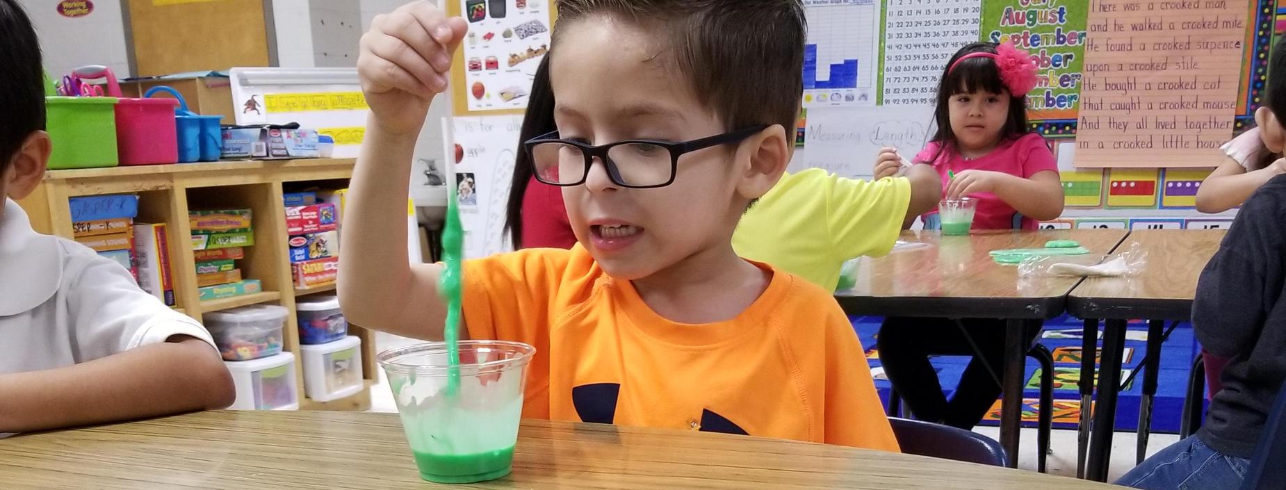 A kindergarten students plays with his green slime creation.