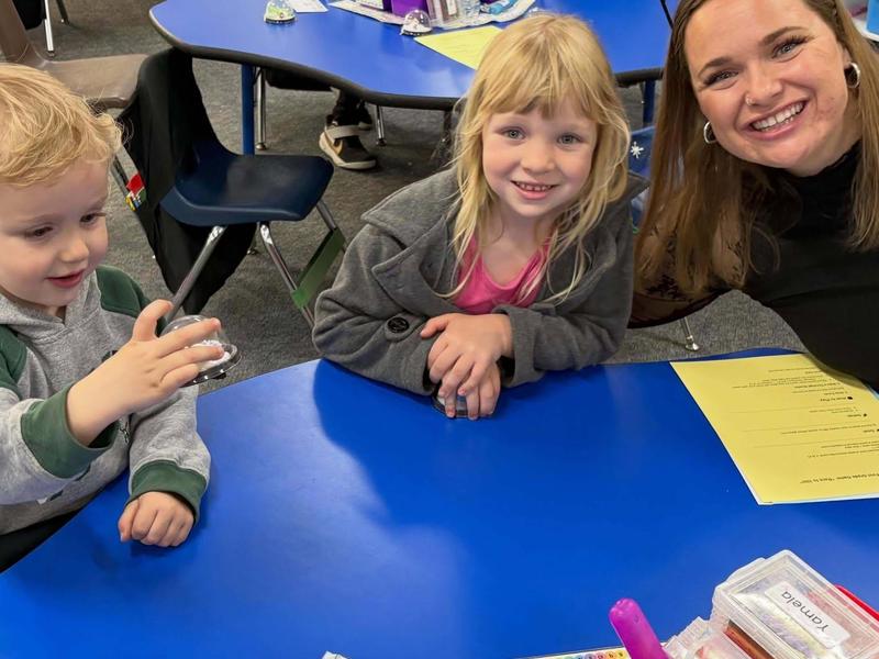 A teacher and two children smiling while sitting at a blue table.