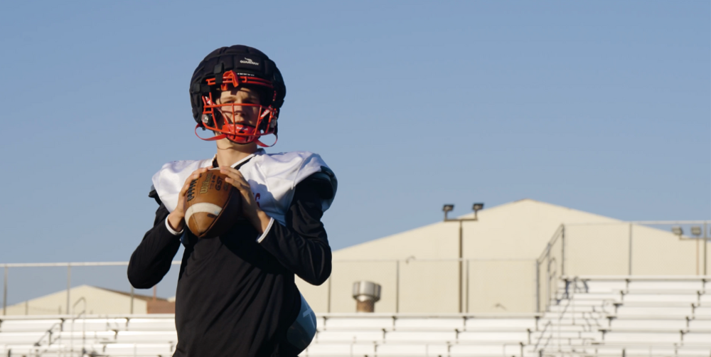 A young football player in uniform poses with a football on a field.