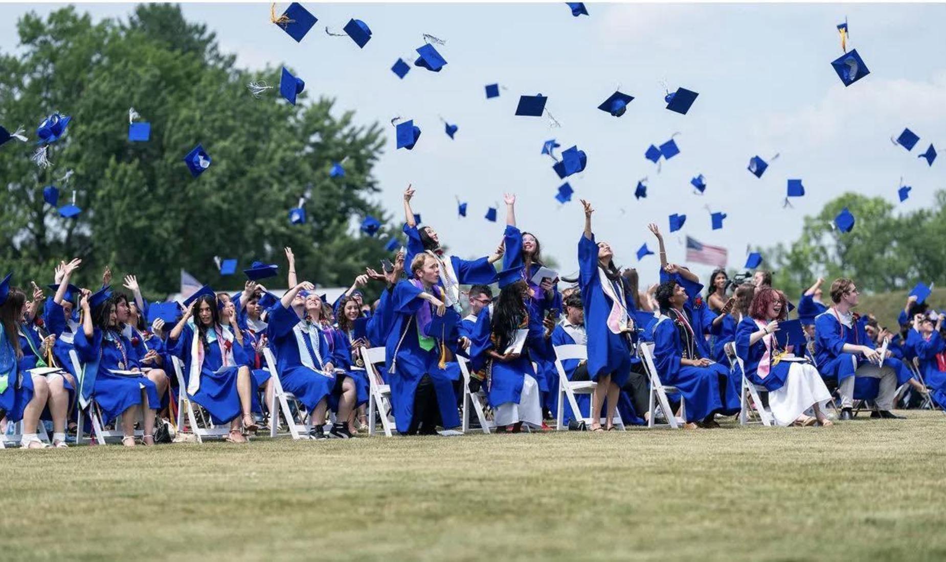 Graduates in blue gowns celebrating by tossing their caps into the air.