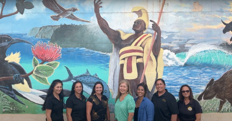 Picture of administrators from all 3 Kohala Schools in front of a mural that includes the Kamehameha Statue, Pololu Valley, and animals/scenery that are important to the Kohala community.