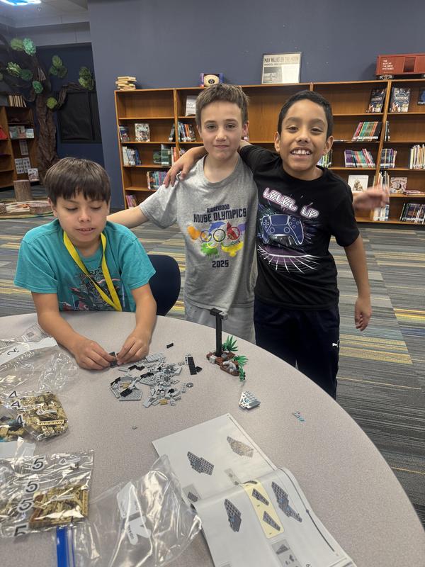 Three students with arms around each other posing next to the LEGO set