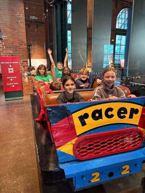 Image depicts a team of Quaker Valley students posing in a car from the rollercoaster "The Racer" from Kennywood at the Heinz History Center.